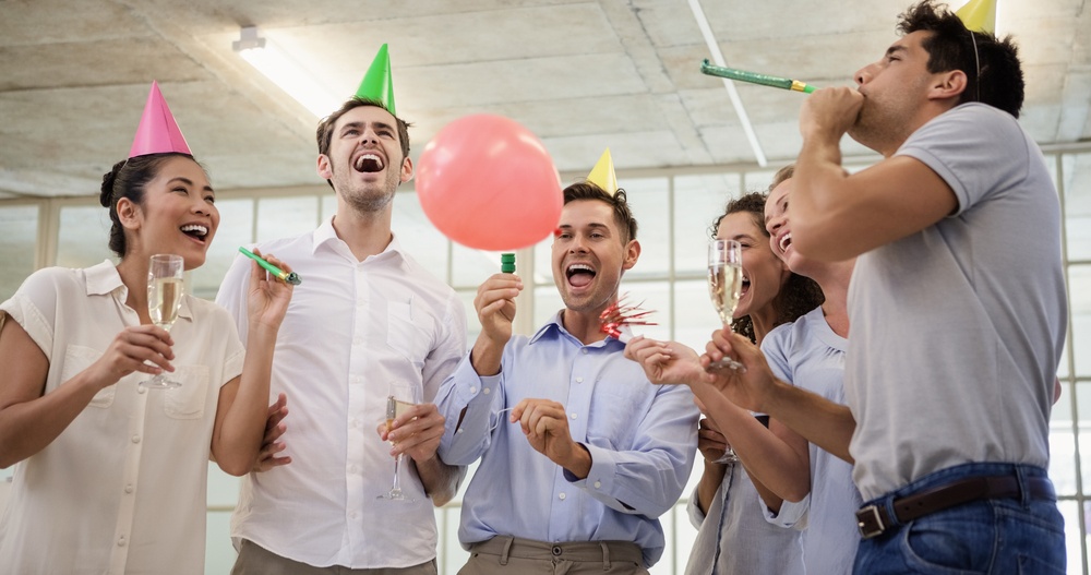 Casual business team celebrating with champagne and party horns in the office